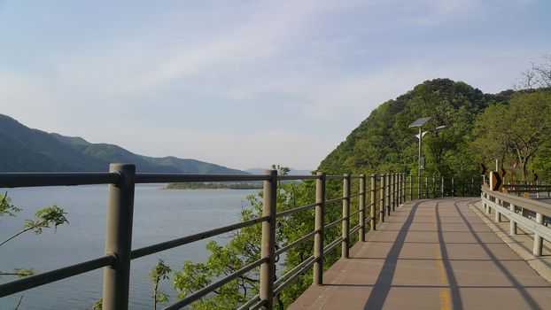 Beautiful view of wooden track for pedestrian exercise and cycling on side of river water and mountains scenery.