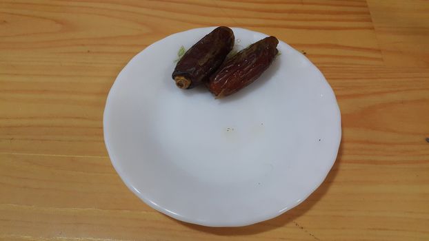 Close up view of fresh dried date palm served in ceramic small white plate over a wooden floor