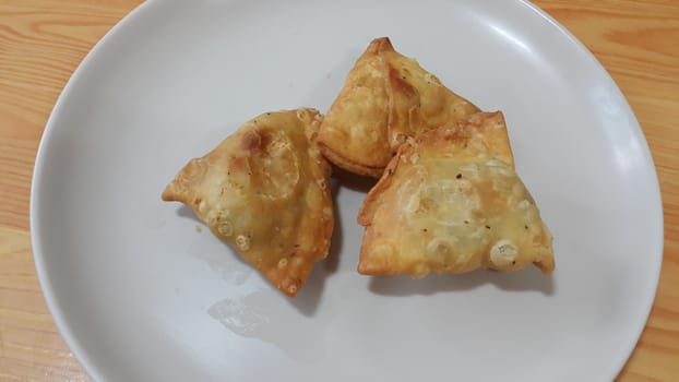 Closeup of delicious home made spicy and crunchy samosa pastries placed in a white ceramic plate on wooden floor