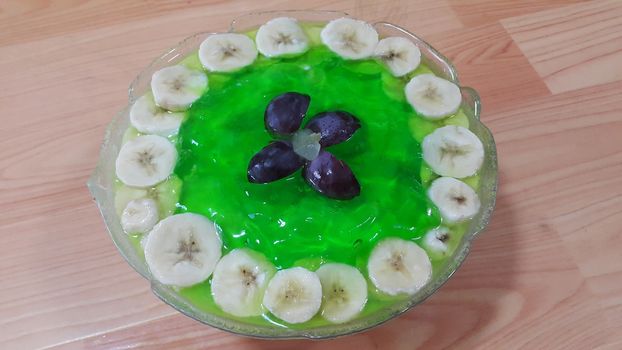 Creamy tasty sweet green jelly over custard with banana slices layered on surface on wooden floor. A top view of home made custard, a dairy products for dessert after meal.