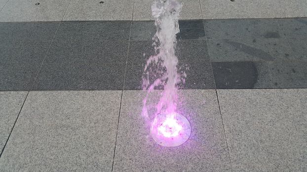 Beautiful and colorful light water fountain over concrete floor. Colorful water shape on fountain with grey background.