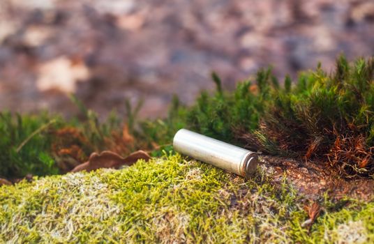 Abandoned electric alkaline battery on the moss in the forest