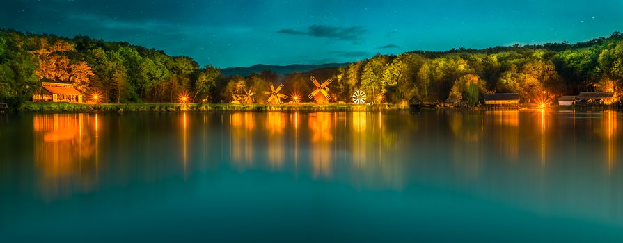 Landscape panorama with windmills at the blue hour in White Night of the Museums. Dumbrava lake, Astra Museum of Traditional Folk Civilization, Sibiu city, Romania
