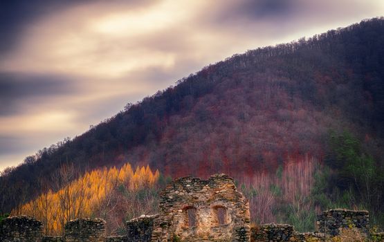 the ruins of an old wall at the foot of a hill in late autumn with clouds