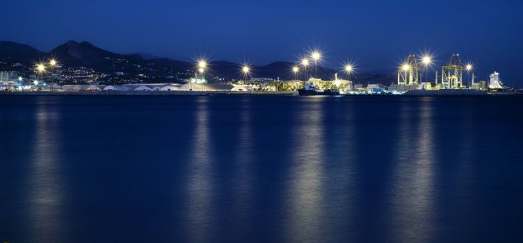 view of Malaga's port, with lights reflecting in the water surface at blue hour, Spain