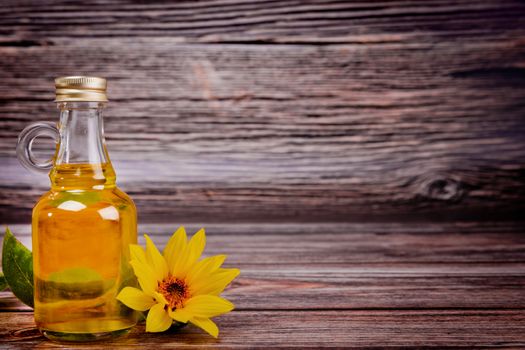 Glass bottle with sunflower oil and flowers on wooden background. Studio shot.