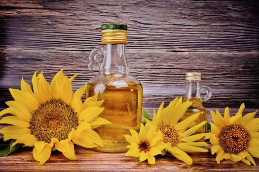 Two glass bottles with sunflower oil and flowers on wooden background. Studio shot.