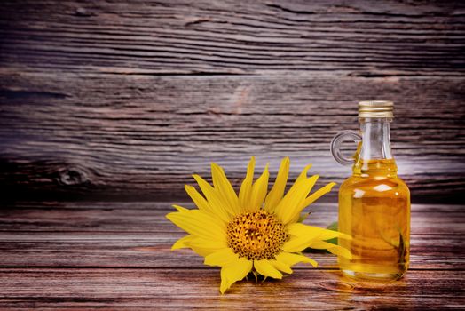 Glass bottle with sunflower oil and sunflower flower on wooden background. Studio shot.