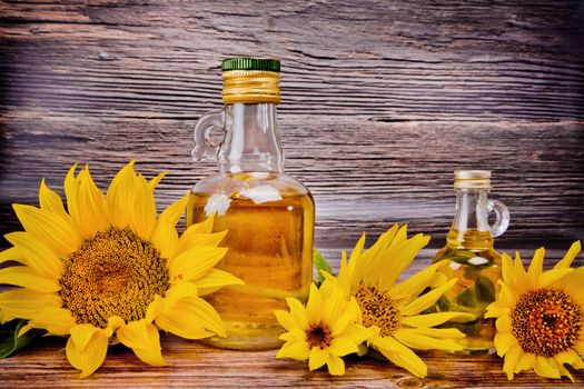 Two glass bottles with sunflower oil and flowers on wooden background. Studio shot.