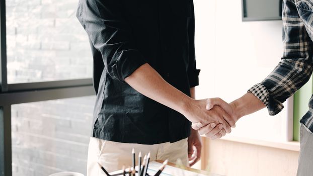 Business people shaking hands at meeting or negotiation, close-up. Group of unknown businessmen and women in modern office at background. Teamwork, partnership and handshake concept
