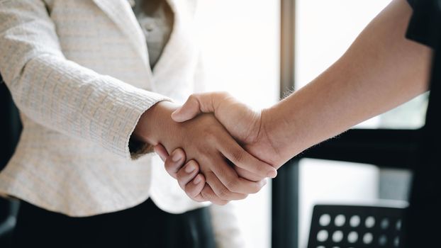 Business people shaking hands at meeting or negotiation, close-up. Group of unknown businessmen and women in modern office at background. Teamwork, partnership and handshake concept
