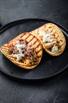 Traditional mexican taco with chicken and beef with ingredients a side on black plate over black textured background side view, selective focus