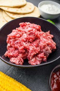 Organic raw minced meat for mexican tacos with vegetables cusine with ingredients in black bowl, over grey textured background, side view