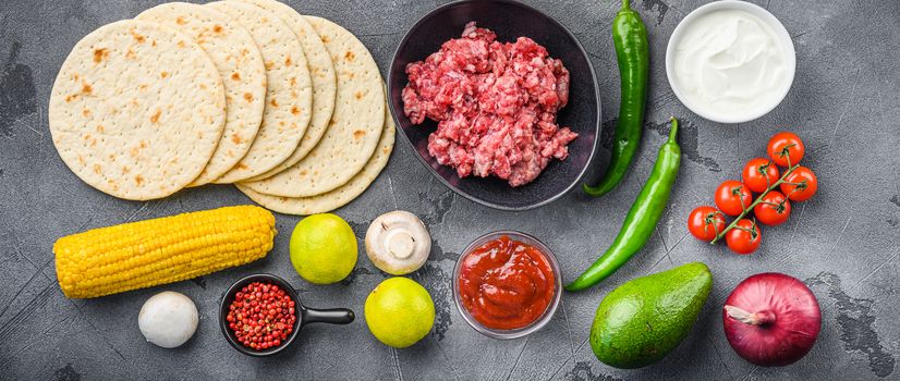 Traditional homemade taco ingredients with meat,salsa, peppers, tomatoes, avocado , corn, tortilla over grey background, top view
