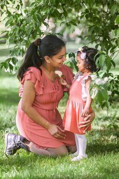 A happy woman in red dress with two years old girl is walking in spring park