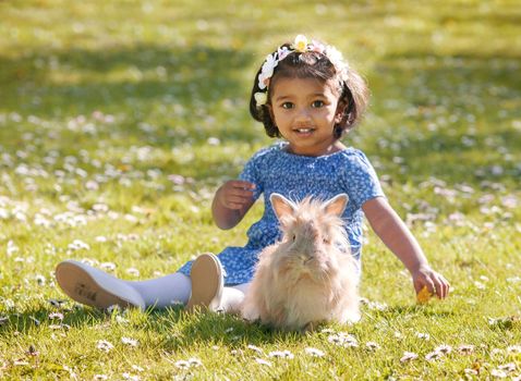 A small Asian girl is sitting with home rabbit on green grass in spring park