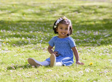 A pretty smile young girl is sitting on green meadow in sunny spring day