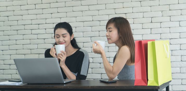 Two interesting Asian women were friends talking about coffee in a coffee shop. Two women sipping coffee And use computer laptops together