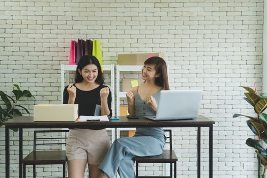 Two Asian female entrepreneurs, an online sales business owner, are chatting and checking orders from customers at home. The beautiful and attractive merchant is smiling happily for the startup.
