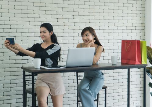 Two interesting Asian women were friends talking about coffee in a coffee shop. Two women sipping coffee And use computer laptops together