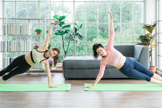 Attractive and healthy women Two Asians Exercising Stretching the muscles with yoga postures together at home. Help balance life