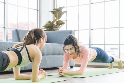 Attractive and healthy women Two Asians Exercising Stretching the muscles with yoga postures together at home. Help balance life