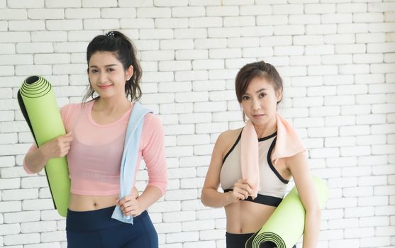 Portrait of a beautiful, attractive, healthy woman, two Asian people With exercise mats Talking in the gym After yoga