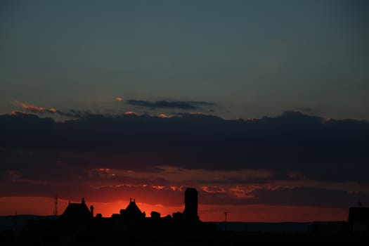 Concept of calm and serenity. Colorful and cloudy sunset in the background. Sibiu, Romania, old medieval town in eastern central Europe. Fiery red sunset with old building silhouette.