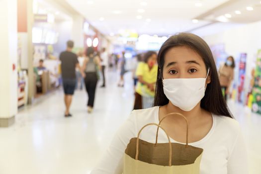 Asian woman long hair wear face mask Holding empty paper shopping bag in supermarket. Girl looking grocery to buy something During coronavirus crisis or covid19 outbreak. new normal concept with copy space.
