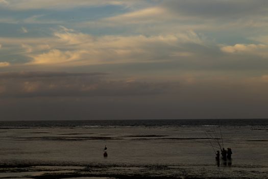 Bali, Indonesia - CIRCA 2018: Group of fisherman fishing for fish in ocean water during sun set with a beautiful colored cloudy sky.