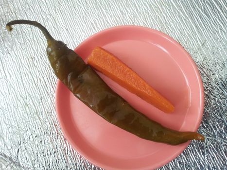 A close up view Green chili pepper with carrot  served in a small plate