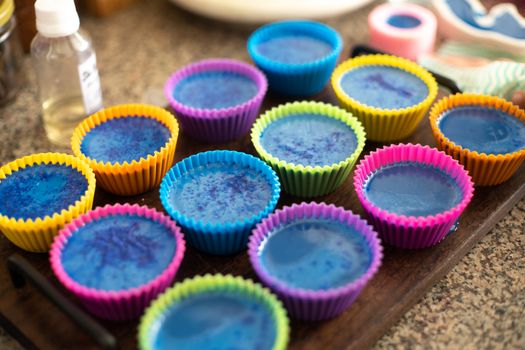 Colorful silicon cupcake molds on wooden coard filled with liquid soap for a home made hobby of melt and pour soapmaking. Shows the beautiful blue glossy liquid used to bake and make cupcakes or muffins.