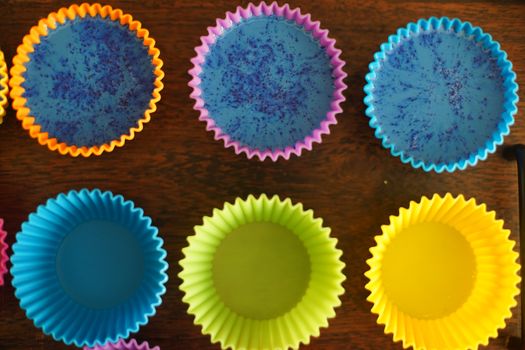 Colorful silicon cupcake molds on wooden coard filled with liquid soap for a home made hobby of melt and pour soapmaking. Shows the beautiful blue glossy liquid used to bake and make cupcakes or muffins.