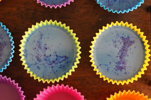 Colorful silicon cupcake molds on wooden coard filled with liquid soap for a home made hobby of melt and pour soapmaking. Shows the beautiful blue glossy liquid used to bake and make cupcakes or muffins.