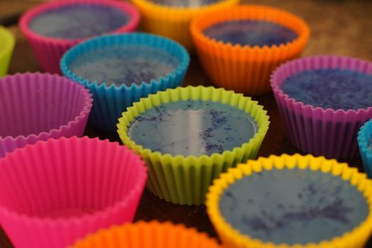 Colorful silicon cupcake molds on wooden coard filled with liquid soap for a home made hobby of melt and pour soapmaking. Shows the beautiful blue glossy liquid used to bake and make cupcakes or muffins.