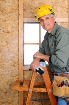 Closeup of  a carpenter leaning on a ladder in front of a wall he is building. Vertical Format.