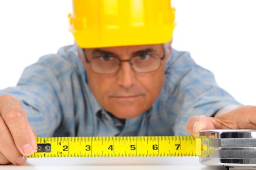 Closeup of a construction worker in hard hat using a measuring tape with the numbers facing forward. Focus is on the mans hands and tape measure.