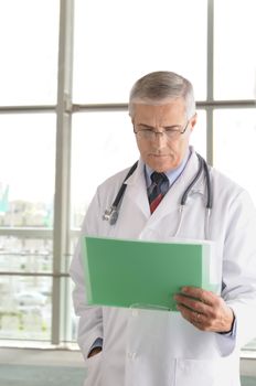 Middle aged doctor reading chart in front of the window of a  modern medical facility