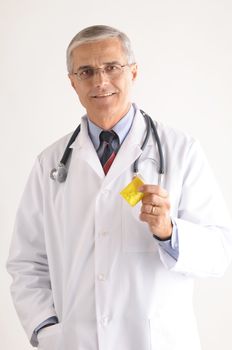 Smiling Middle Aged Doctor holding prescription bottle on gray background vertical format