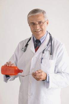Smiling Middle Aged  Doctor in Labcoat with Stethoscope Pouring Medicine from a Bottle onto a Spoon, vertical