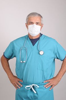 Middle Aged  Doctor in Scrubs and Surgical Mask with Hands on Hips, vertical on gray background