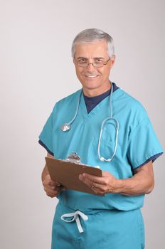 Smiling Middle Aged  Doctor in Scrubs Reading a Patients cart on his clipboard
