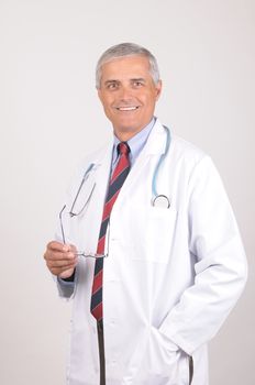 Smiling Middle Aged  Male Doctor in Lab Coat with Stethoscope Holding his eye glasses- gray background