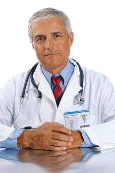 Middle aged doctor in lab coat sitting at table with his hands together. Closeup in vertical format on a white background.