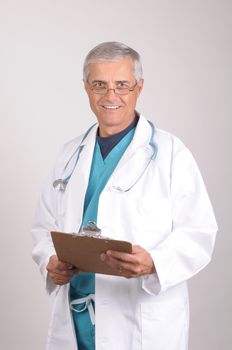 Smiling Middle Aged  Doctor in Scrubs and Lab Coat with clipboard -vertical composition on gray background