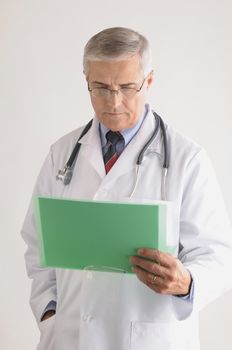 Middle Aged  Doctor in Lab Coat and Stethoscope Looking at a Patients Chart vertical format over gray background