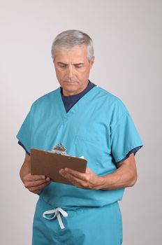 Middle Aged  Doctor in Scrubs Reading a Patients cart on his clipboard