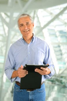 Closeup of a casual businessman in a modern factory setting holding a tablet computer. Vertical Format.