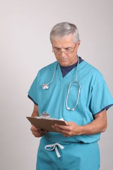 Middle Aged  Doctor in Scrubs Reading a Patients cart on his clipboard