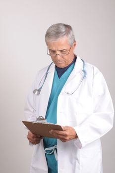 Middle Aged  Doctor in Scrubs and Lab Coat Reading chart on clipboard -vertical composition on gray background